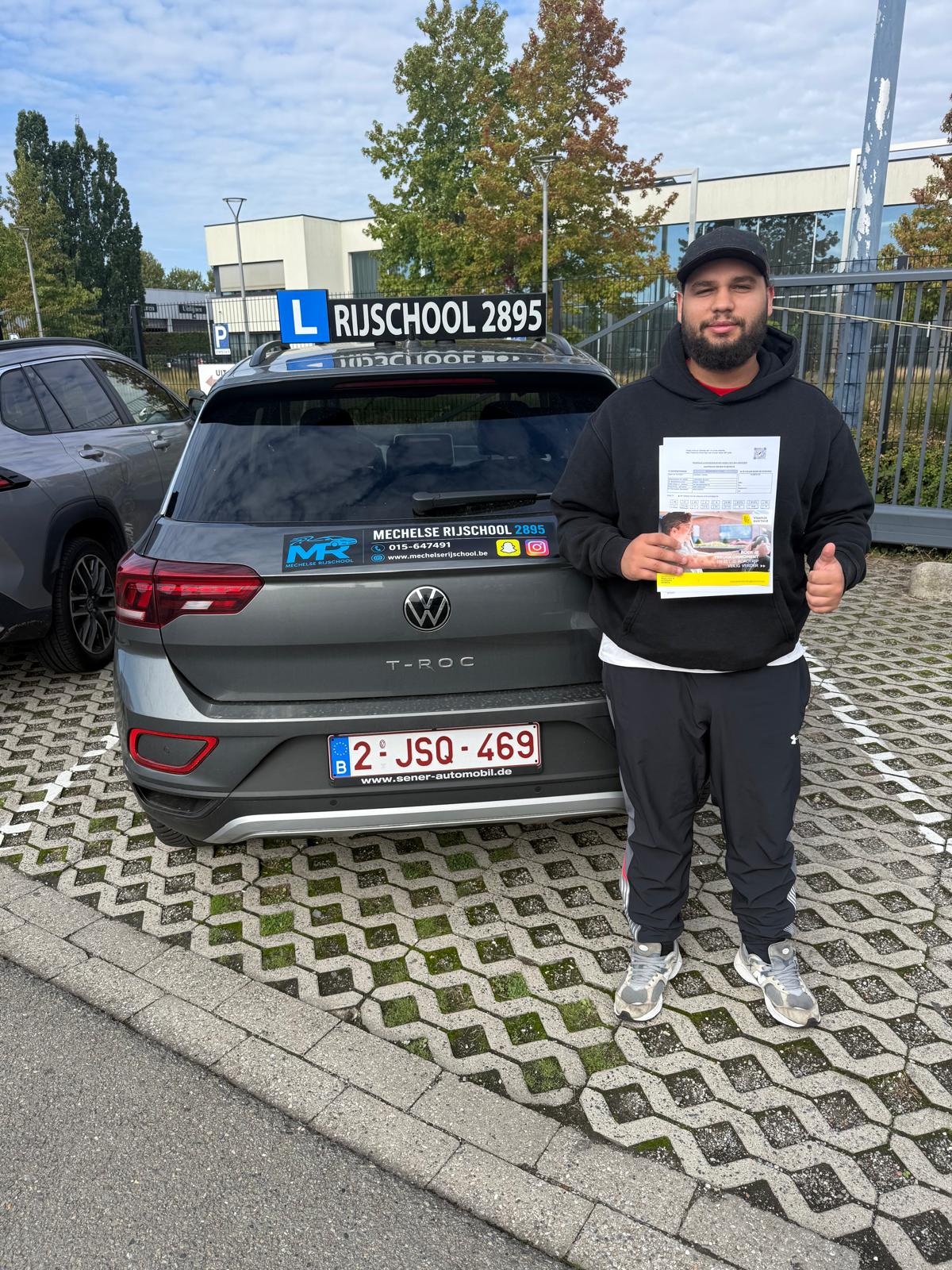 Trotse leerling met een duim omhoog naast de Volkswagen lesauto